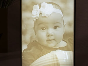 Lighted 3D printed lithophane picture box with image of a baby. Framed in black.