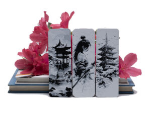 Japanese art inspired bookmarks sitting on a book with bright pink azaleas behind them.