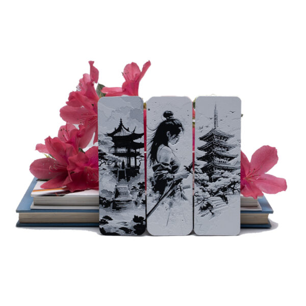 Japanese art inspired bookmarks sitting on a book with bright pink azaleas behind them.