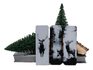 3 bookmarks wit bucks and stags in natural setting sitting on a stack of books with wood and evergreen trees behind them.