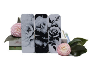 Set of three floral bookmarks propped in front of books and pink Camillas.