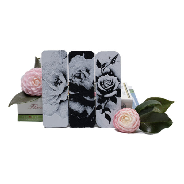 Set of three floral bookmarks propped in front of books and pink Camillas.