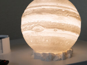 3D printed Jupiter table lamp illuminated on rocky base.