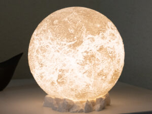 Moon lamp sitting on a side table, resting on a rocky base brightening up the corner of a white room.