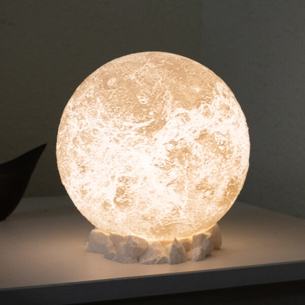 Moon lamp sitting on a side table, resting on a rocky base brightening up the corner of a white room.