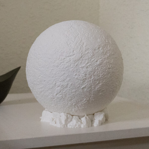 Moon lamp sitting on a side table, resting on a rocky base not lighted but all white showing the craters and textures of the moon.